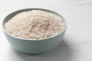 Photo of Raw basmati rice in bowl on white marble table, space for text