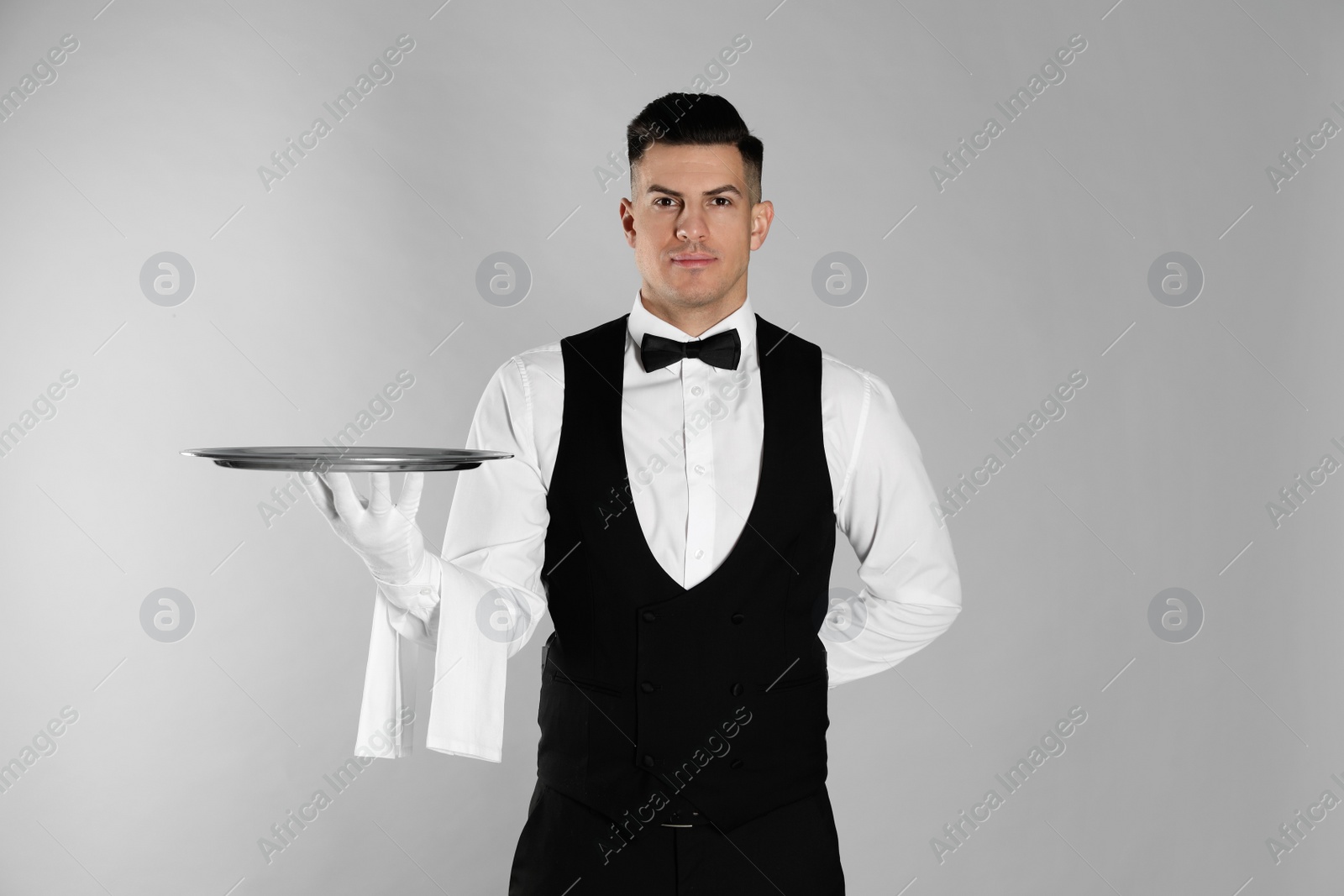 Photo of Handsome butler with tray on light grey background