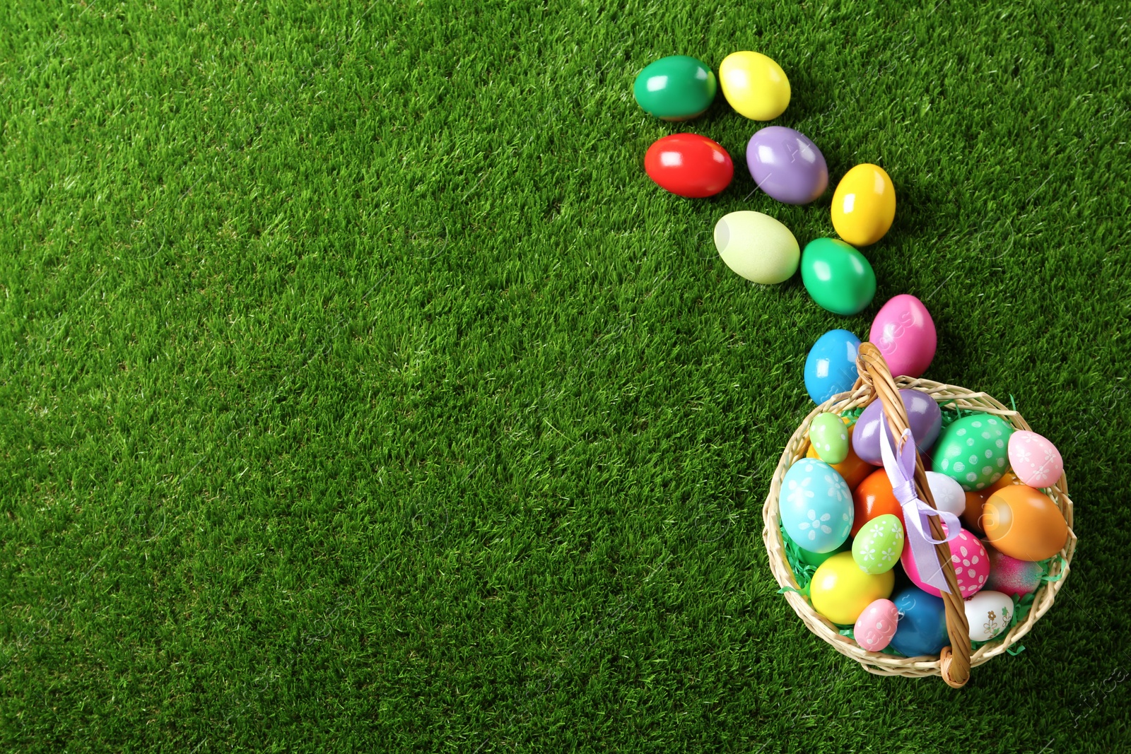 Photo of Wicker basket with Easter eggs on green grass, flat lay. Space for text