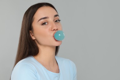 Beautiful woman blowing bubble gum on grey background. Space for text
