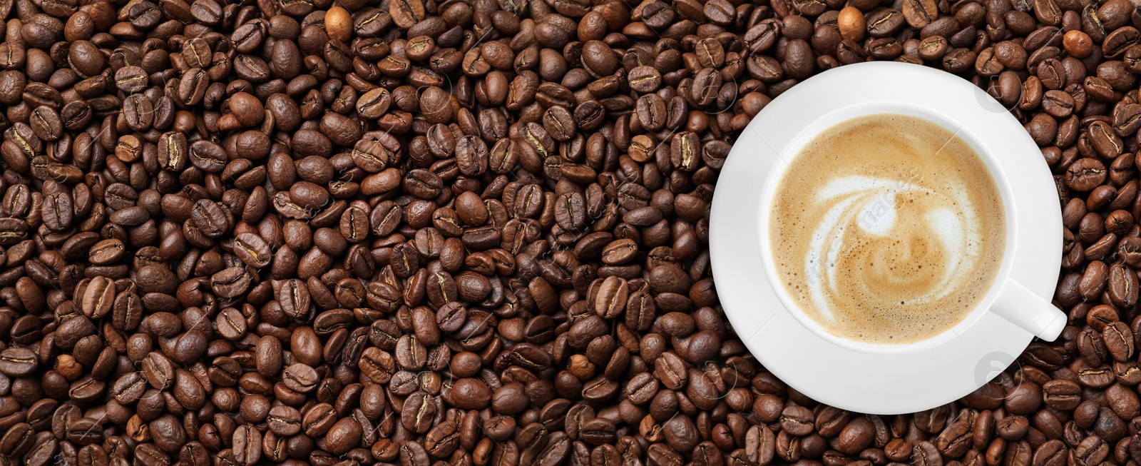 Image of Cup of tasty aromatic coffee on roasted beans, top view. Banner design