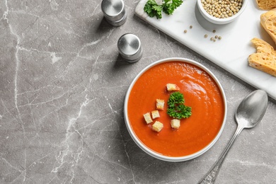 Photo of Bowl of fresh homemade tomato soup and space for text on grey table, top view