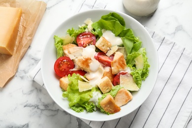 Photo of Delicious fresh Caesar salad in bowl on white marble table, flat lay