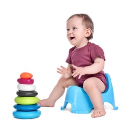 Photo of Little child with toy pyramid sitting on baby potty against white background