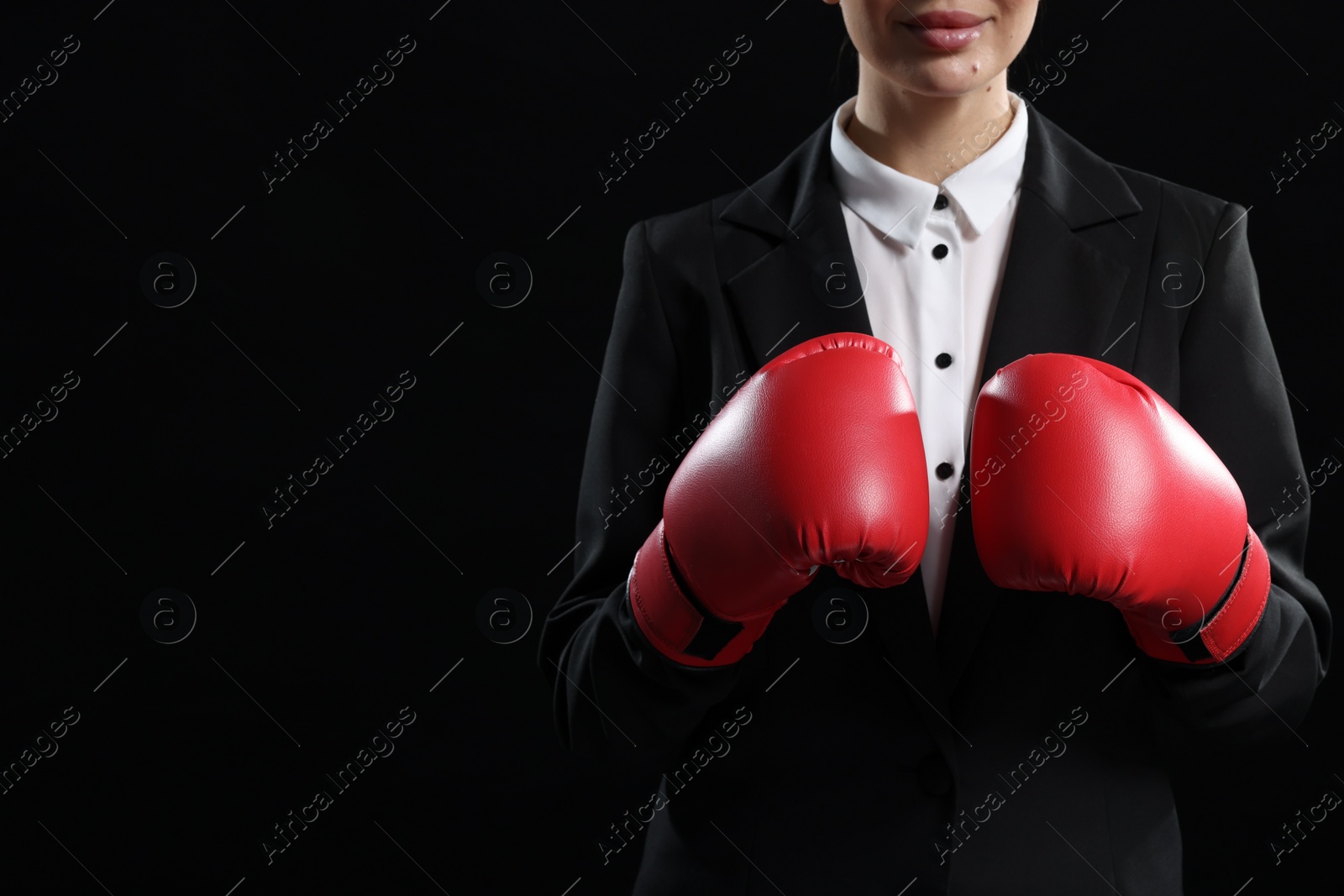 Photo of Businesswoman in suit wearing boxing gloves on black background, closeup. Space for text