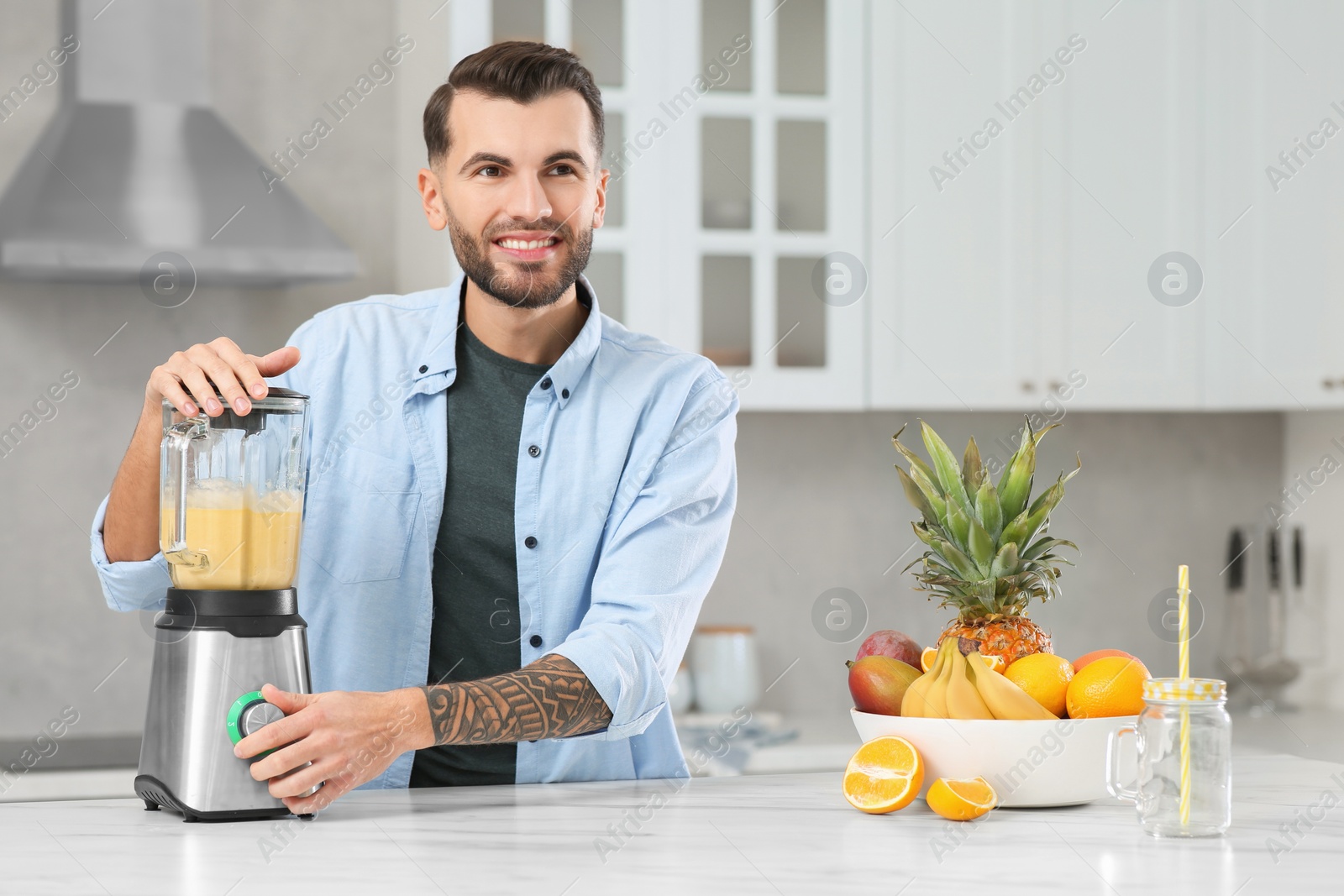 Photo of Handsome man preparing ingredients for tasty smoothie at white marble table in kitchen