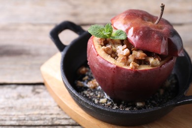 Tasty baked apple with nuts, honey and mint in baking dish on wooden table, closeup