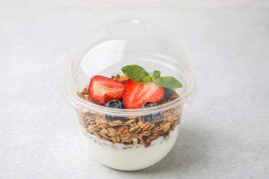 Photo of Tasty granola with berries and yogurt in plastic cup on light table, closeup