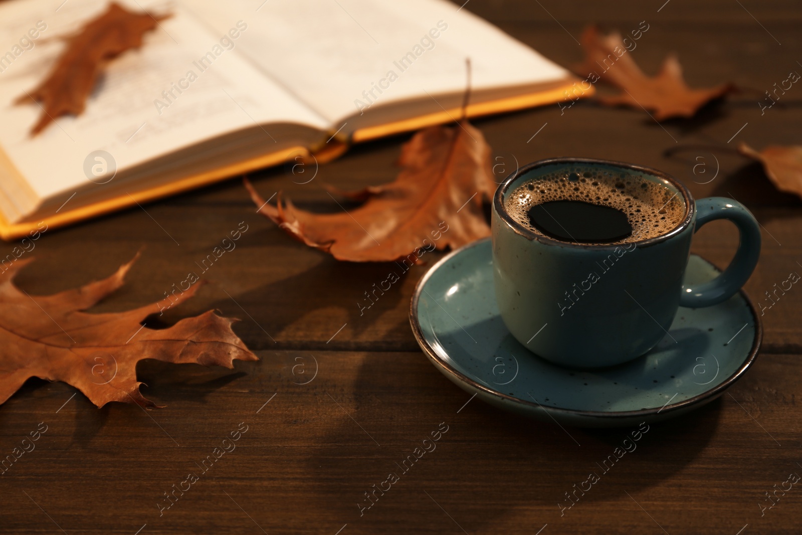 Photo of Cup of aromatic coffee, book and autumn leaves on wooden table. Space for text