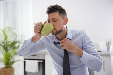 Sleepy man with cup of drink at home in morning