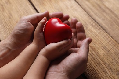 Photo of Father and his child holding red decorative heart at wooden table, closeup