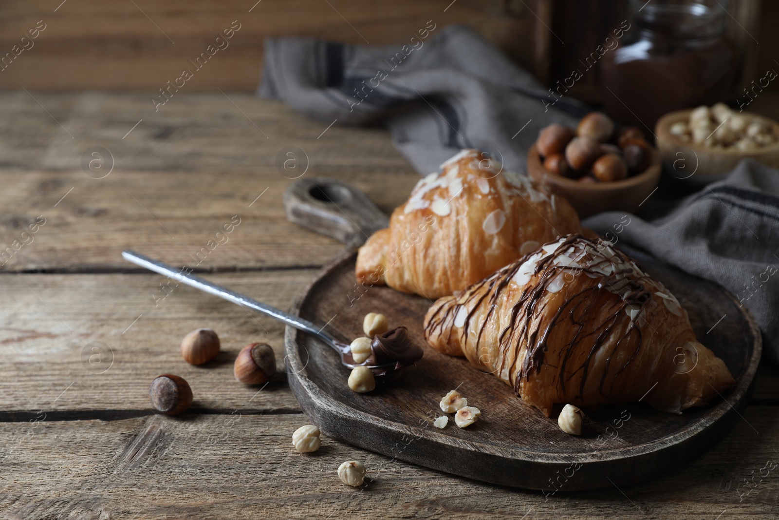 Photo of Delicious croissants with chocolate and nuts on wooden table, space for text