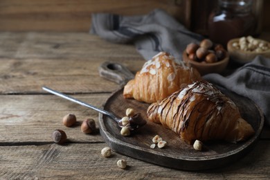 Photo of Delicious croissants with chocolate and nuts on wooden table, space for text