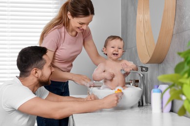 Photo of Father and mother washing their little baby in sink at home