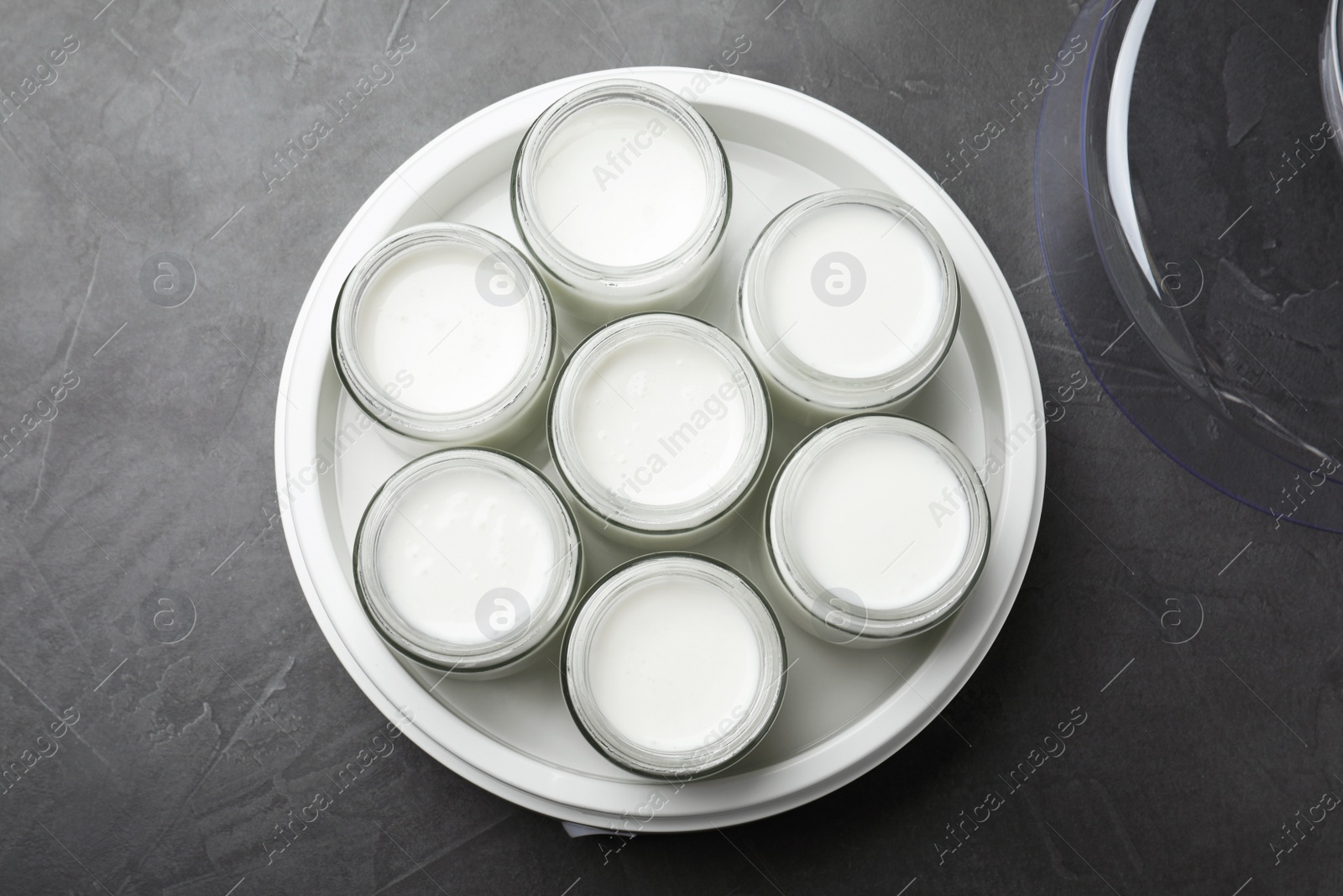 Photo of Modern yogurt maker with full jars on dark grey table, top view