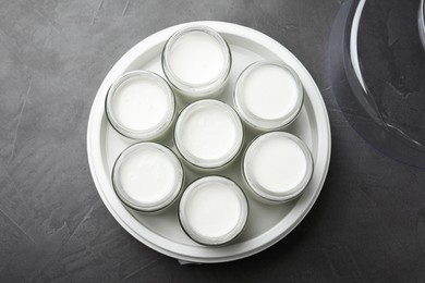 Modern yogurt maker with full jars on dark grey table, top view