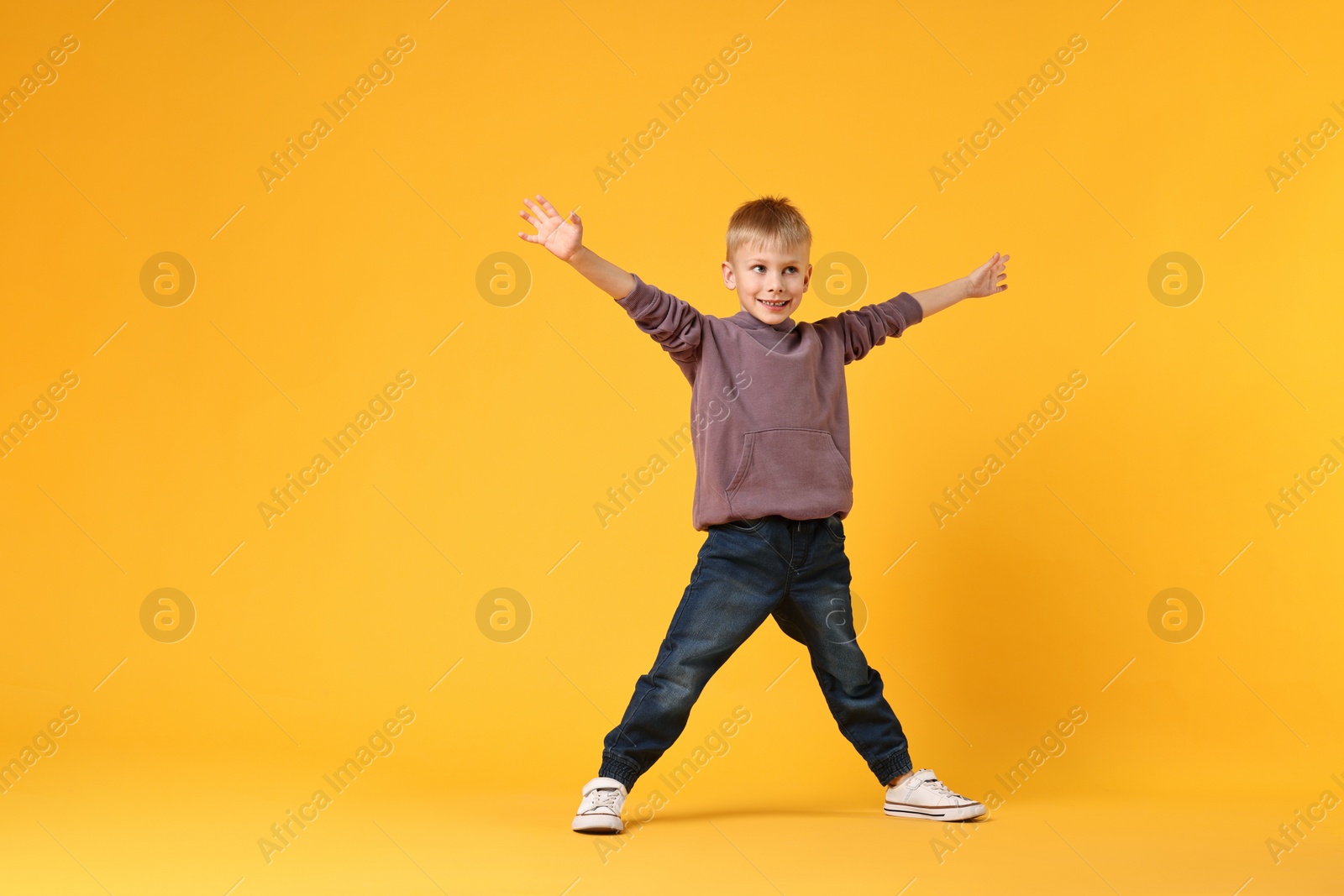 Photo of Happy little boy dancing on yellow background. Space for text