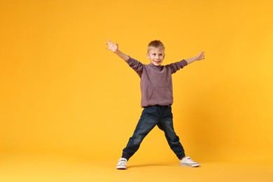 Happy little boy dancing on yellow background. Space for text