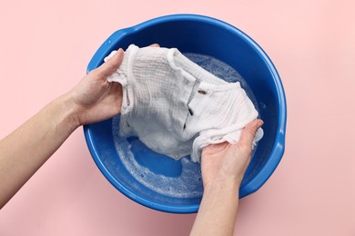 Woman washing baby clothes in basin on pink background, top view