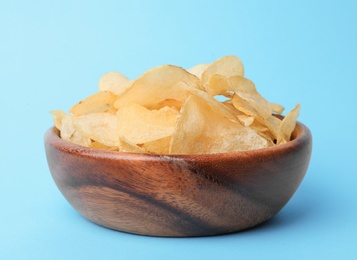 Delicious crispy potato chips in bowl on color background