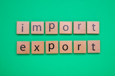 Photo of Words Import and Export made of wooden squares on green background, top view