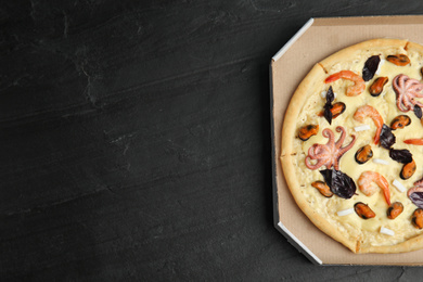 Photo of Delicious seafood pizza  in cardboard box on black table, top view. Space for text