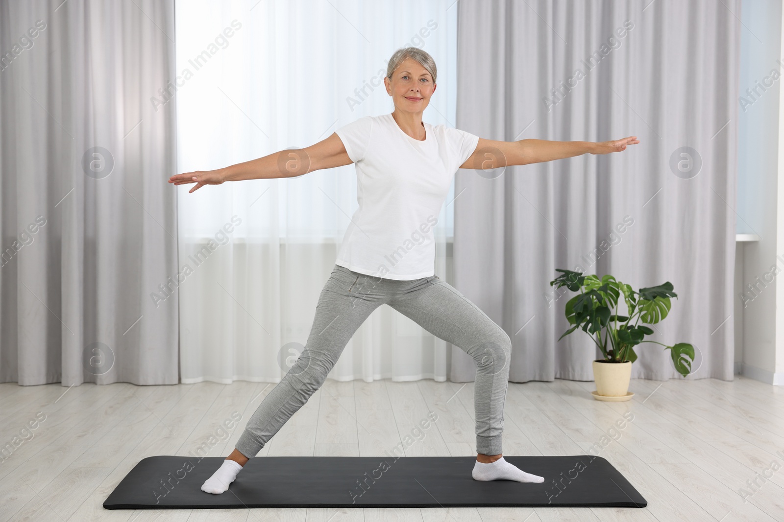 Photo of Happy senior woman practicing yoga on mat at home