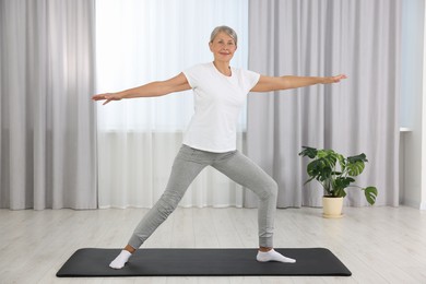 Happy senior woman practicing yoga on mat at home