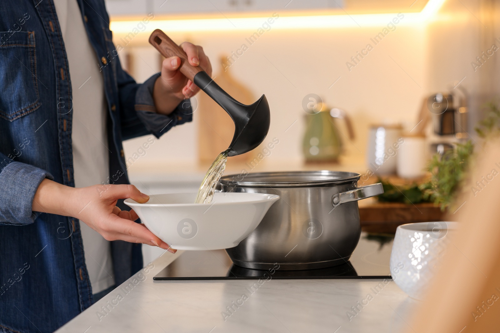 Photo of Woman pouring tasty soup into bowl at countertop in kitchen, closeup