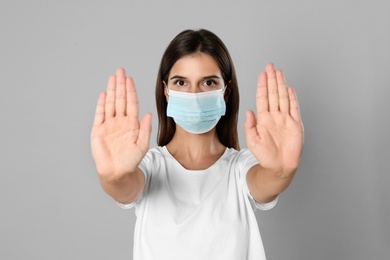 Photo of Woman in protective mask showing stop gesture on grey background. Prevent spreading of coronavirus