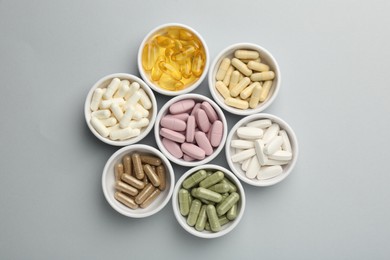 Different vitamin pills in bowls on grey background, flat lay