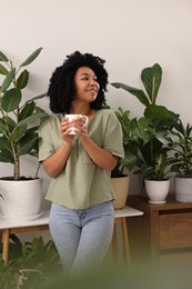 Relaxing atmosphere. Happy woman with cup of hot drink near beautiful houseplants in room