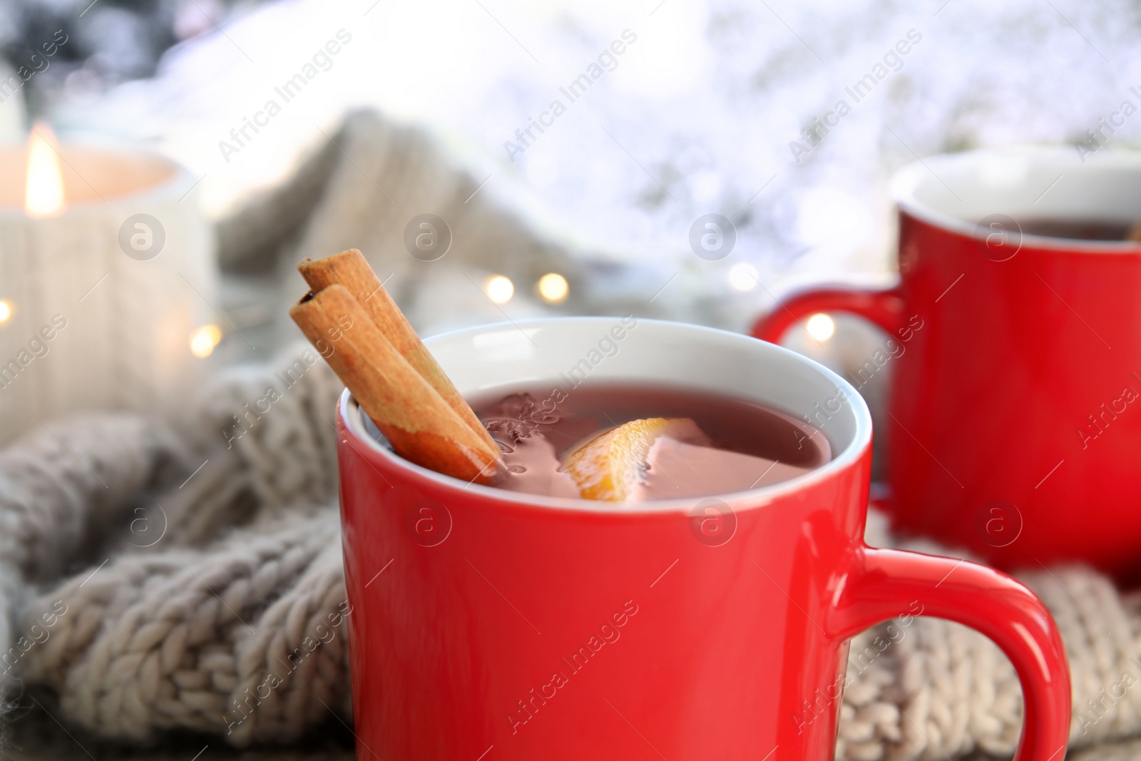 Photo of Cups of hot winter drink with scarf on window sill indoors, closeup