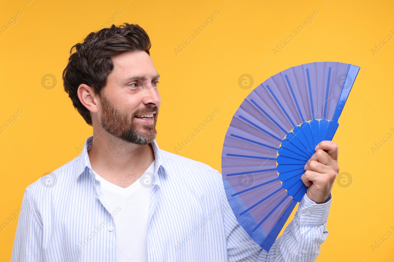 Photo of Happy man holding hand fan on orange background