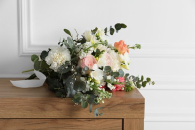 Bouquet of beautiful flowers on wooden table near white wall