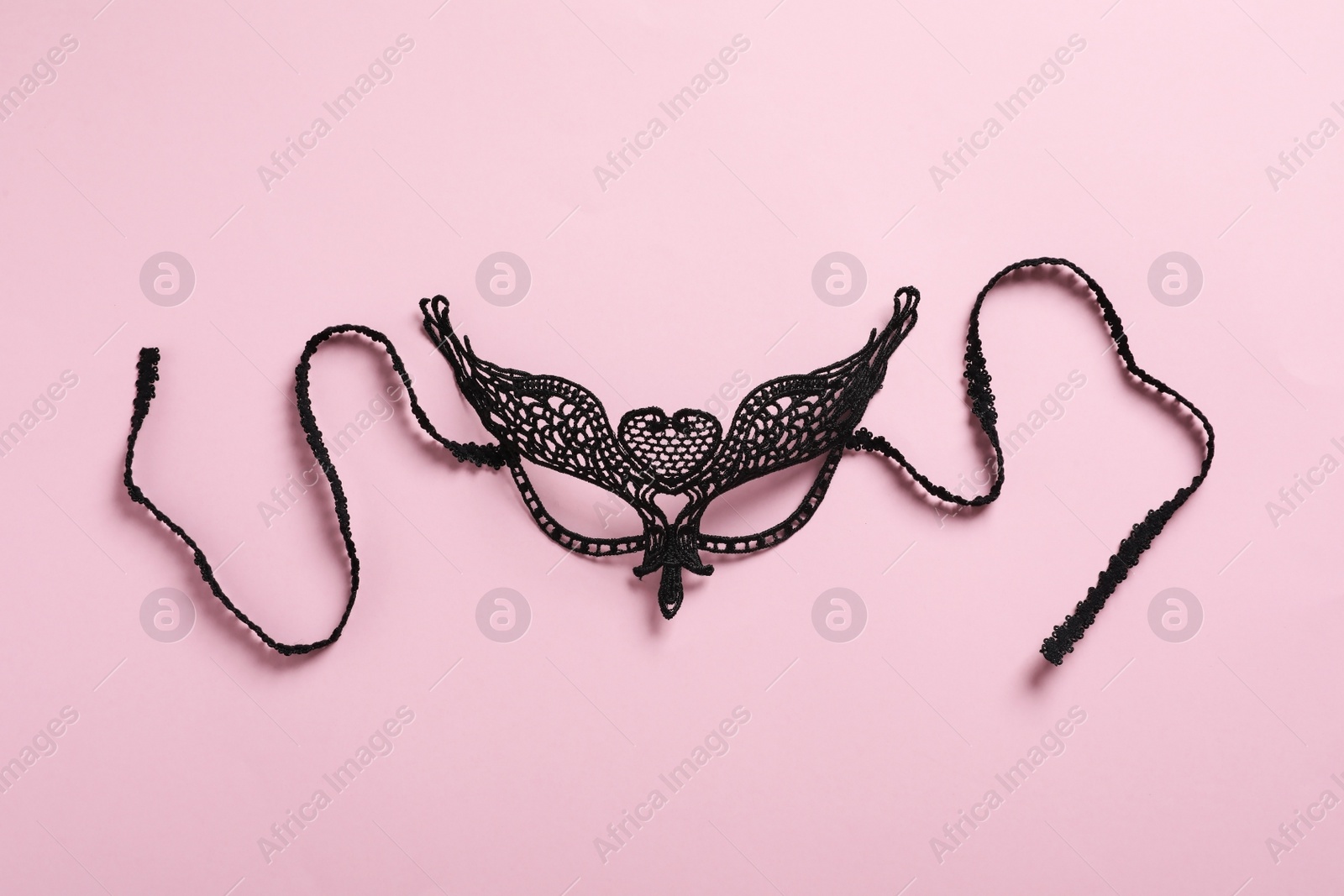 Photo of Black lace mask for sexual role play on pink background, top view