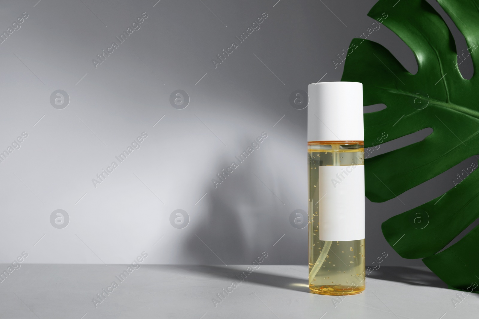 Photo of Bottle of cosmetic product and green palm leaf on table against light background, space for text