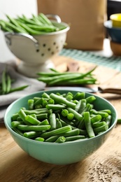 Photo of Fresh green beans in bowl on wooden table, closeup. Space for text