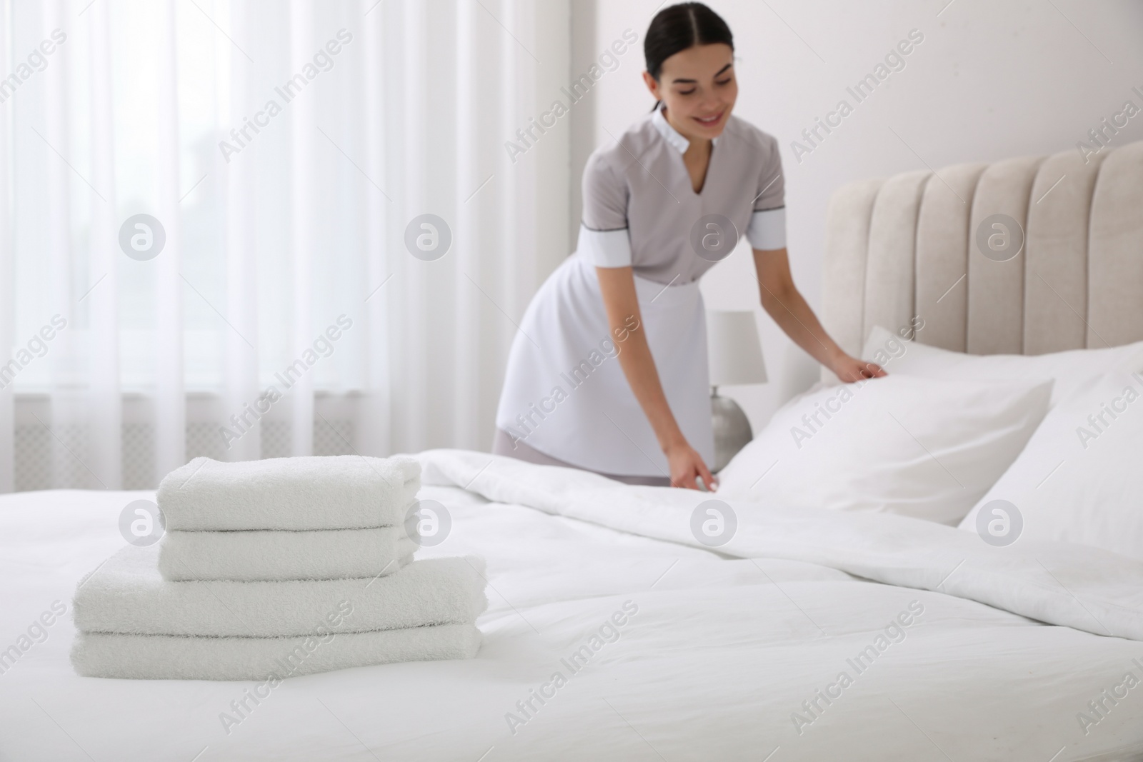 Photo of Chambermaid making bed in hotel room, focus on fresh towels. Space for text