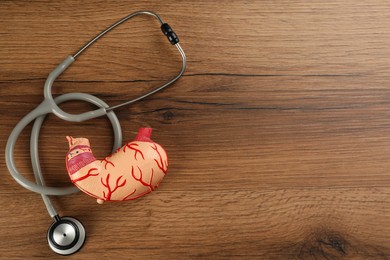 Photo of Human stomach model and stethoscope on wooden table, flat lay. Space for text