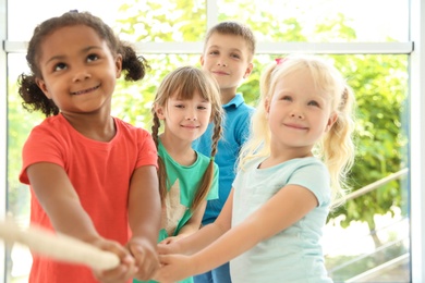 Photo of Little children pulling rope with hands indoors. Unity concept