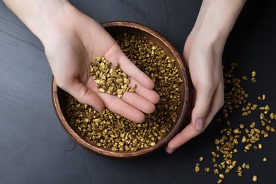 Woman with gold nuggets at black table, top view