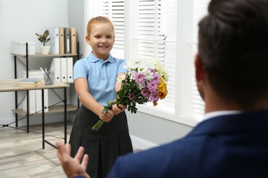 Photo of Schoolgirl with bouquet congratulating her pedagogue in classroom. Teacher's day