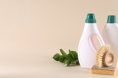 Photo of Bottles of cleaning product, sponge, brush and floral decor on beige background. Space for text