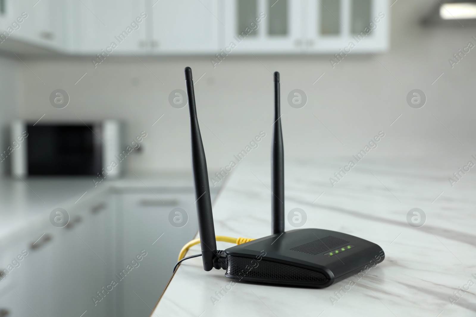 Photo of Modern Wi-Fi router on white marble table in kitchen