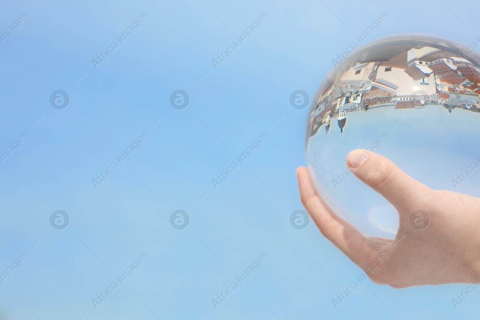 Photo of View of beautiful city street, overturned reflection. Man holding crystal ball against sky, closeup. Space for text