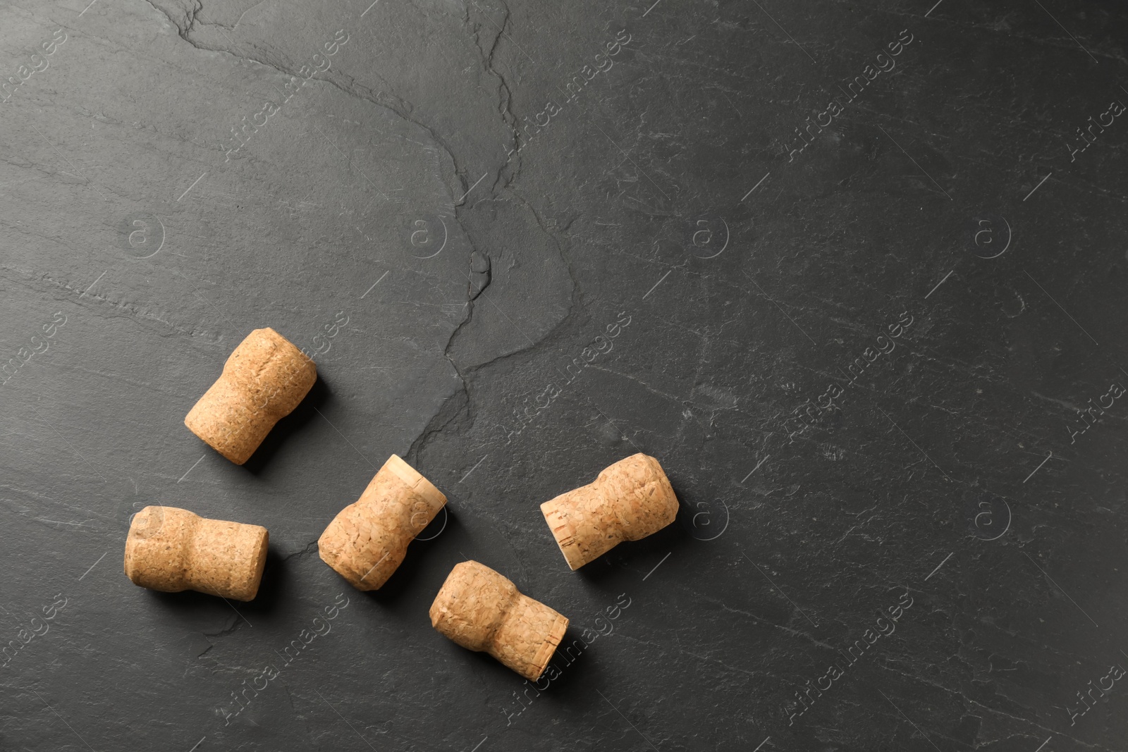 Photo of Sparkling wine corks on black table, flat lay. Space for text