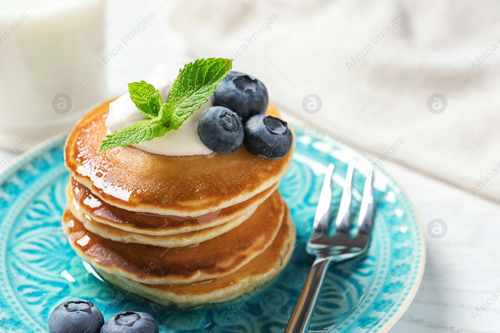 Photo of Plate of tasty pancakes with blueberries, sauce and mint on white wooden table, closeup