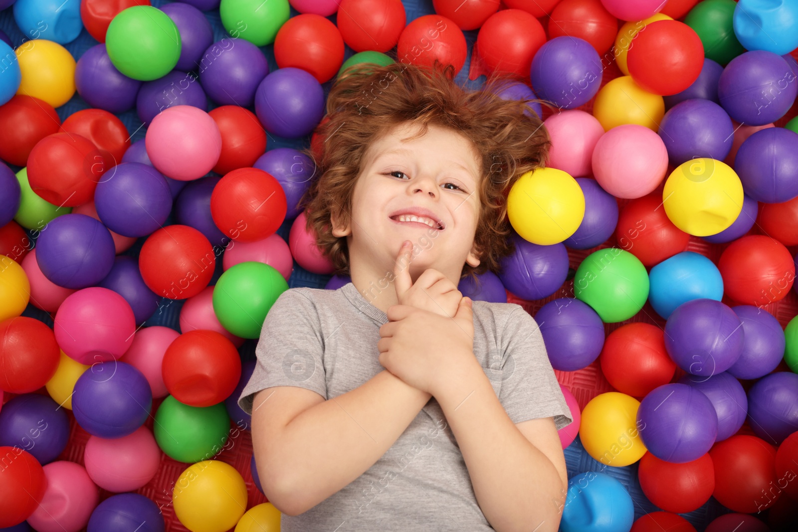 Photo of Happy little boy lying on many colorful balls, top view