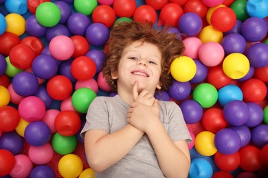Photo of Happy little boy lying on many colorful balls, top view